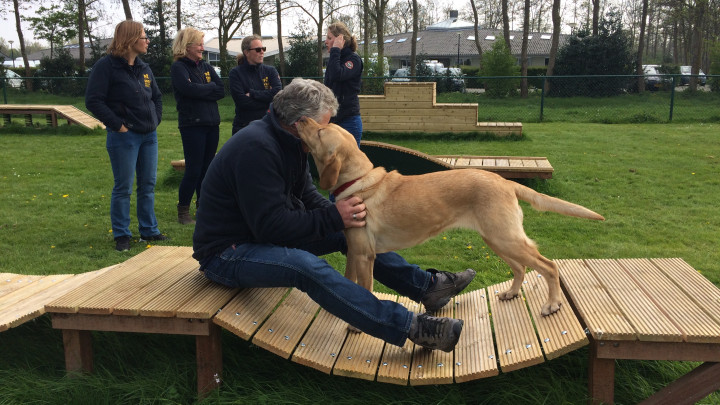 Hoofdinstructeur Kees Tinga en geleidehond in opleiding bij de nieuwe speeltoestellen gesponsord door Rabobank Coöperatief Fonds en ING Nederland Fonds