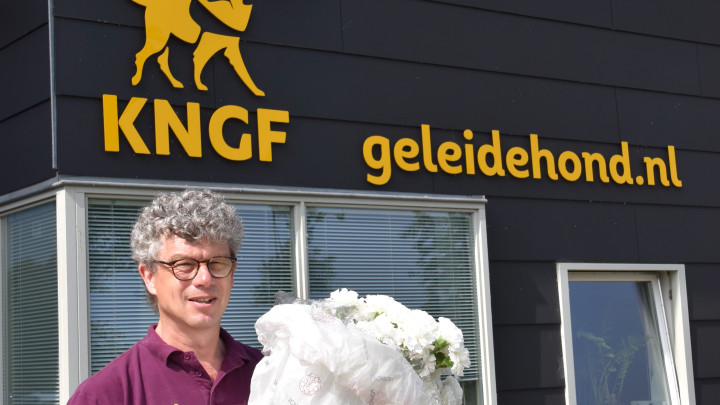 Herman staat voor het KNGF Geleidehonden gebouw met een bos prachtige witte anjers in zijn handen.